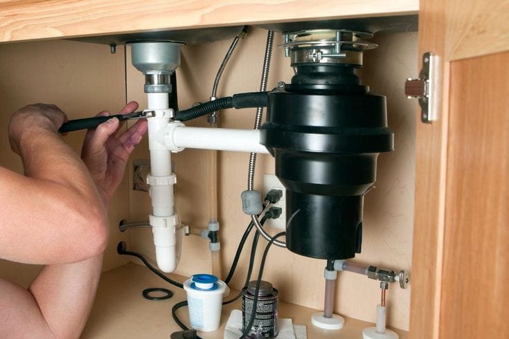 Plumber installing a garbage disposal beneath a kitchen sink in Albany